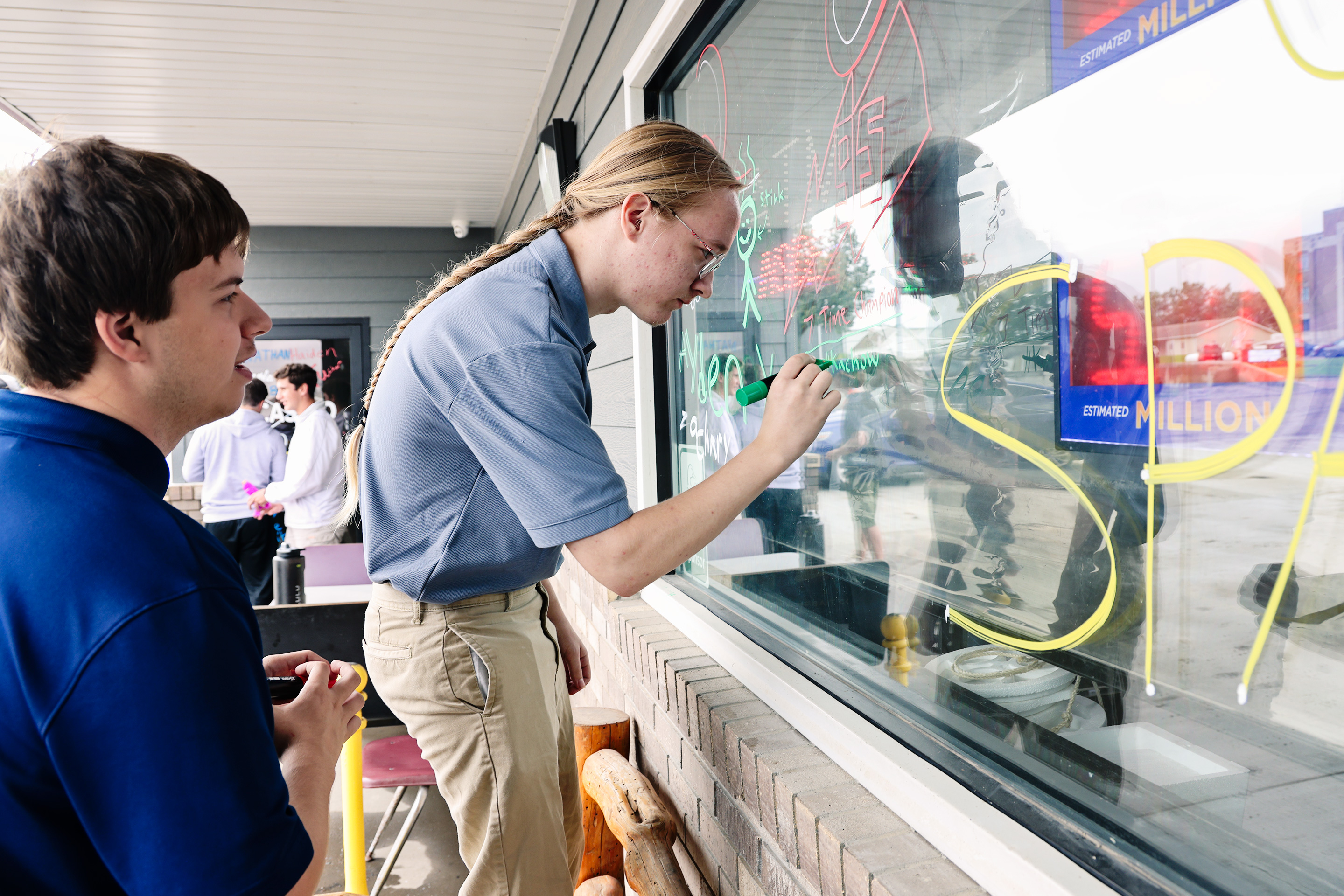 Jerrytt Culver and Zachary Kruse were among the Wessington Springs High School seniors who filled the Humm-Dinger storefront windows with names and Homecoming messages Tuesday after rain washed away their traditional Sunday night street whitewashing. Store Manager Ellen Tobin offered the windows to the students after learning Mother Nature had erased their handiwor