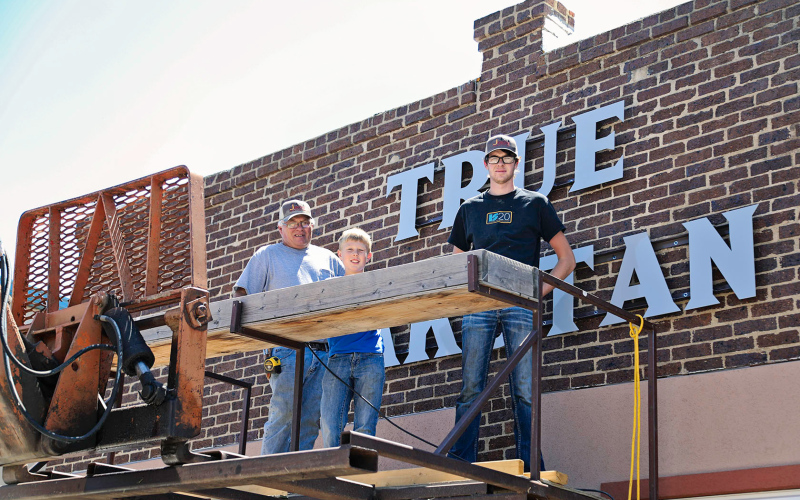 Craig Jensen, his grandson Sutten and Jensen Construction employee Xavier Baysinger made quick and precise work of hanging the metal sign made by the welding outfit at Spring Valley Colony.      