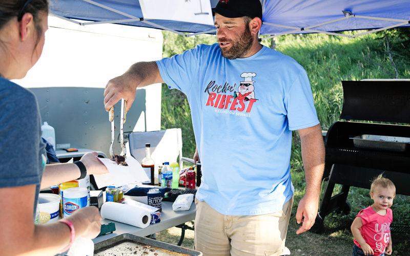 Rockin’ Ribfest contestant Eric Shroeder serves up a sample to a hungry customer as daughter Hazel looks on.