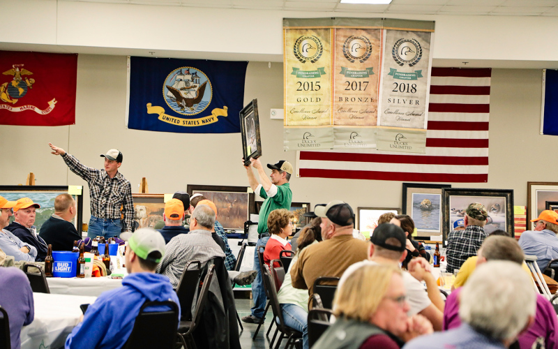 Auctioneer Clayton Keck (left) and Tom Mebius are shown during the live auction. Banners touting national recognition for the local chapter were displayed. The chapter recently received the top honor of “Elite” status for its work during 2021.