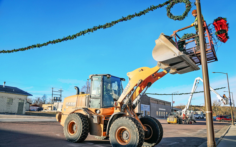 City workers strung the town’s beloved Christmas garland across Main Street Monday. Pictured are Jim Vavra (inside loader) and Robert Wenzel (in the bucket). KRISTI HINE / TRUE DAKOTAN
