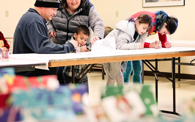 While families waited for their visit with Santa, they enjoyed coloring Christmas pages provided by WS Senior Center volunteers. In the foreground are goody bags filled and donated to the Santa Saturday event by the Dennis and Sandy Beckman family. Each child who visits Santa leaves with their own bag of treats.  Volunteers also decorated by Santa’s chair and served a free will meal during the visit.
