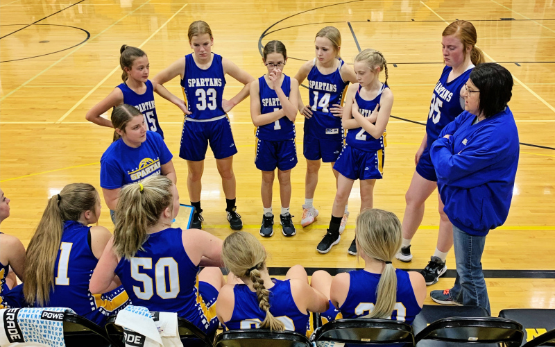 Kirstie Munsen (kneeling at left) is shown during girls junior high basketball action. For her senior project, she assisted in coaching the junior high Spartans girls alongside head coach Liza Kolousek (right).