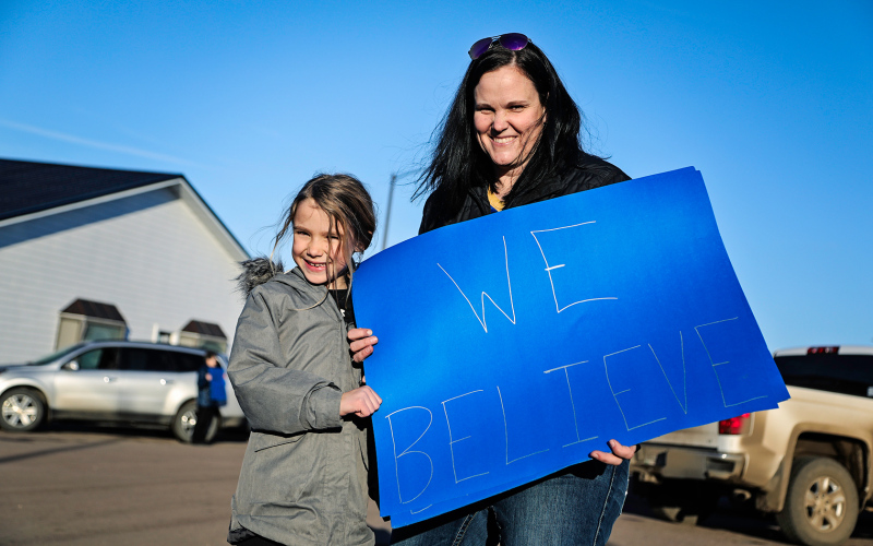 Erin Yost and daughter Remi hold a “We Believe” sign, inspired by the Lady Spartans 1999 trip to state that Yost was a part of as a player.