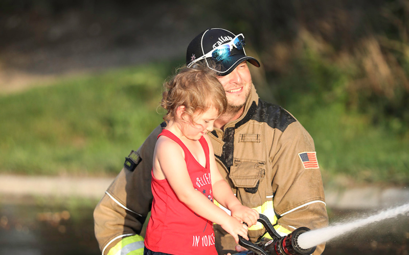 Fire Chief Jim Vavra helps Bristol Grohs during the friendly water barrel fight with fireman Cody Barber (not pictured).