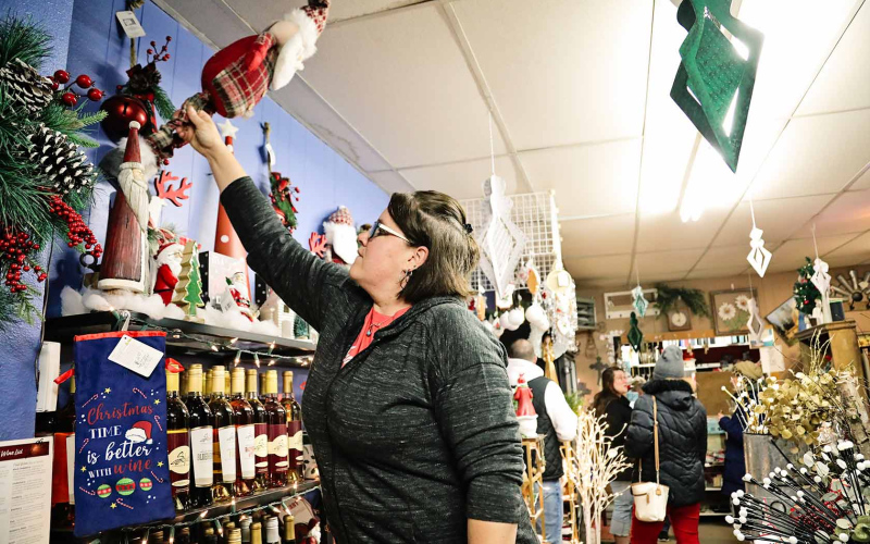 Laura Baker of Baker’s Design pulls a tall Santa off the shelf for a customer during Holiday Spectacular.