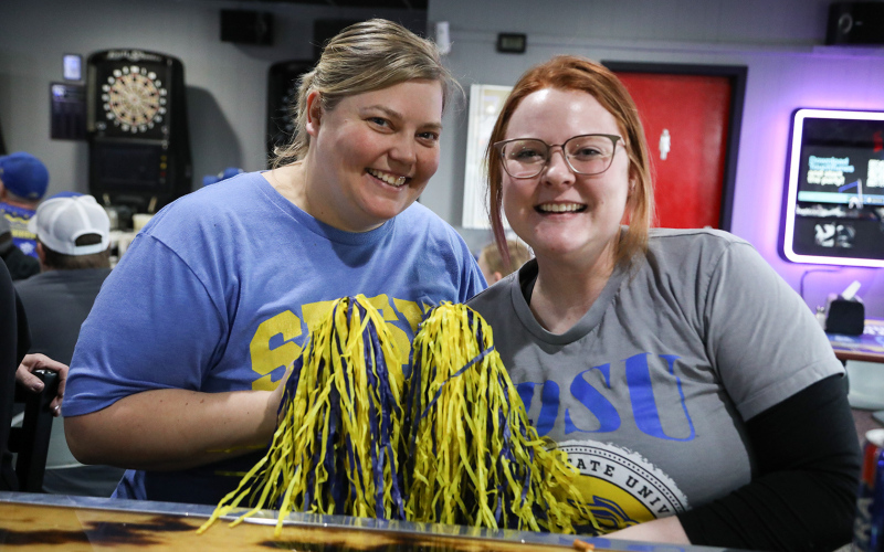 With pom poms at the ready, Pin Twisters owner Betsy Schroeder (left) and Kaci Anson cheer on the Jacks.