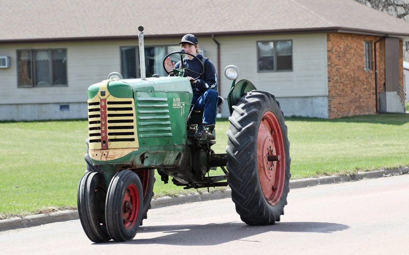 Kordell Schafer drove an Oliver in the parade, shown heading east along 2nd Street. The route took the parade by the elementary school and nursing home, then proceeded west on Main Street to head south on Dakota Avenue to the large American Legion parking lot “up on the hill” at the entrance to town.
