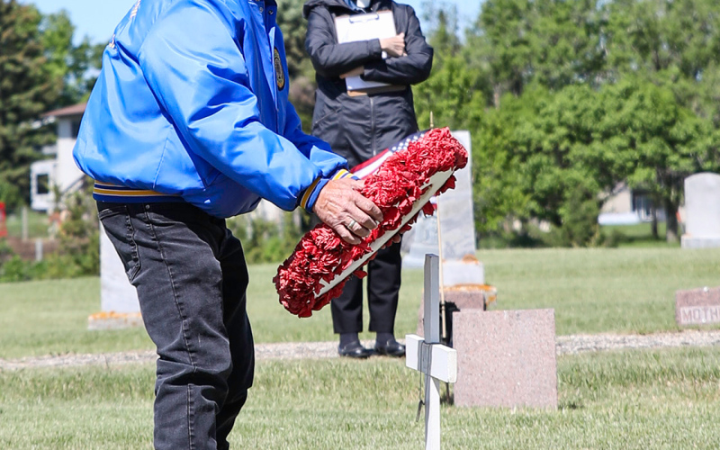 Darrold Rounds places a wreath of poppies during the Prospect Hill Memorial Day program. The speaker for the program, Our Saviors Lutheran Church Pastor Nancy Rieke, looks on.
