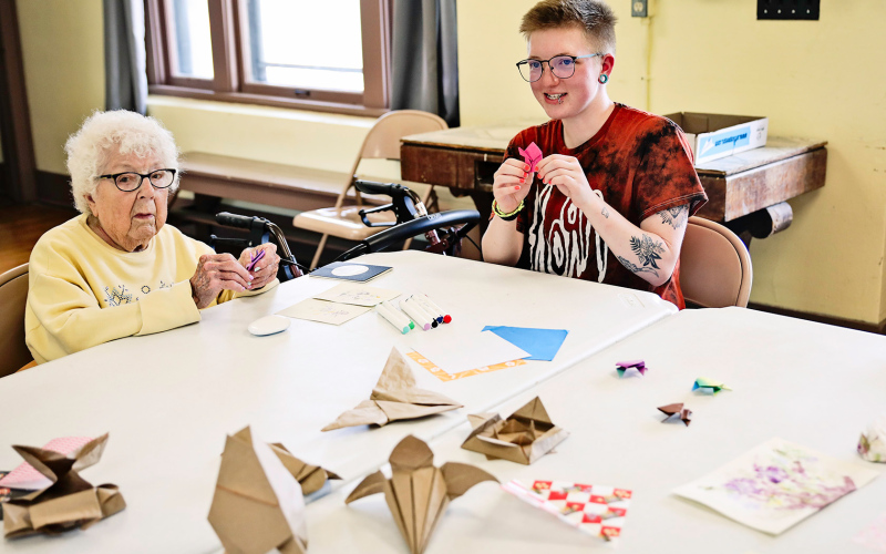 Faith Easter leads an origami class. Class attendee Peg Olson is pictured at left.