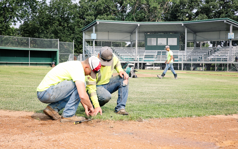 City of Wessington Springs employees Dylan Schimke and Lucas VanEnglenburg (foreground) work to repair a sprinkler at David Jost Memorial Field in preparation for this weekend’s amateur baseball district tournament. Cade Mohling (background) walks toward the mound to continue valve repairs. KRISTI HINE / TRUE DAKOTAN