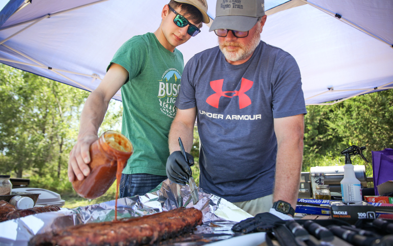 Father-son team Chris and Austin Schimke work together to apply homemade barbecue sauce.