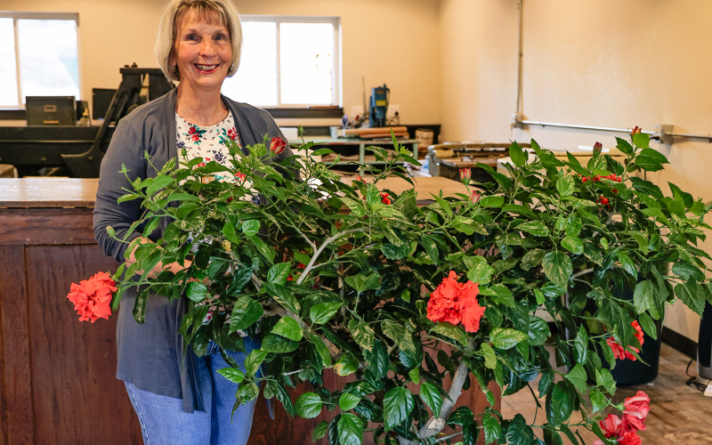 Delia Atkinson, True Dakotan Office Manger stands alongside the hibiscus tree she nurtured for nearly 10 years.