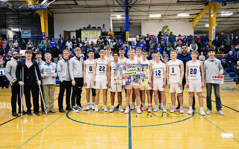 KRISTI HINE / TRUE DAKOTAN Wessington Springs High School junior Parker Graff (center), standing with his teammates and coaches in front of a home crowd, proudly displays a 1,000 point banner shortly after achieving the milestone at last week’s 70-31 victory over Hitchcock-Tulare.