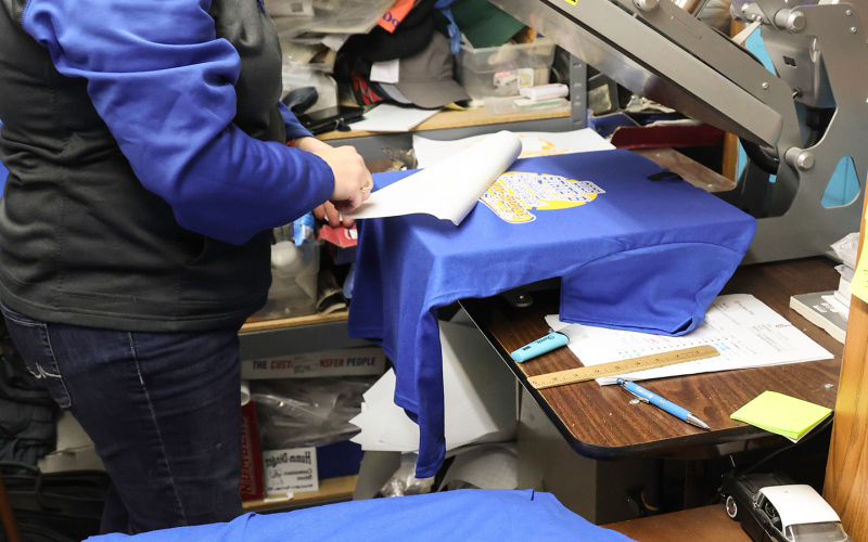 Laura Baker of Baker’s Design was busy screenprinting over 300 official State B 2025 shirts in her Main Street shop.