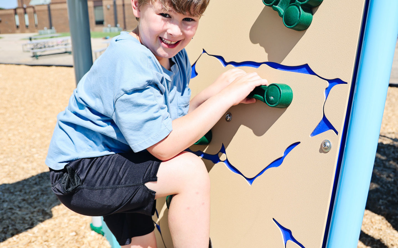 Tucker Graff flashes a big smile while climbing the rock wall on the new playground.