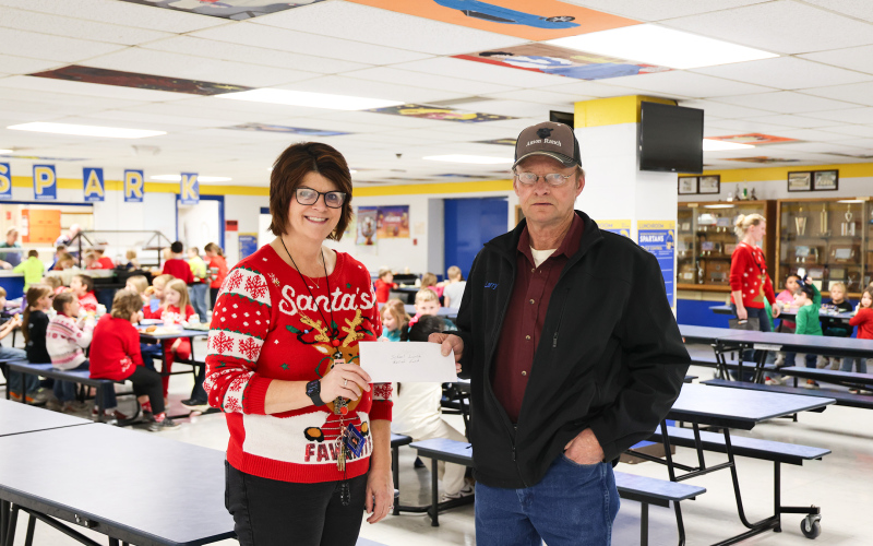 Wessington Springs resident Larry Powell presents a check for more than $3,500 to Wessington Springs Elementary School Principal Becky Fjerstad in the WSES lunchroom. The funds were raised through Christmas train rides during the town-wide holiday kickoff on Dec. 1. Proceeds from the rides were donated to the Wessington Springs School District lunch program to help cover the cost of additional servings for students. (KRISTI HINE / TRUE DAKOTAN)