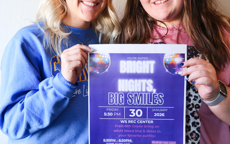 Wessington Springs High School students Kendall Kolousek, left, and Tierney Knipfer hold a flyer for Bright Nights, Big Smiles, a family engagement event they are organizing through the school’s FCCLA chapter. The glow-themed event will be held Jan. 30 at the WS Rec Center. (KRISTI HINE / TRUE DAKOTAN)