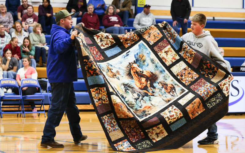 JR Hine and Micah Orth hold up a handmade quilt during the live auction at Ella Fagerhaug’s senior project fundraiser. The quilt was a major contributor to the night’s total donations.