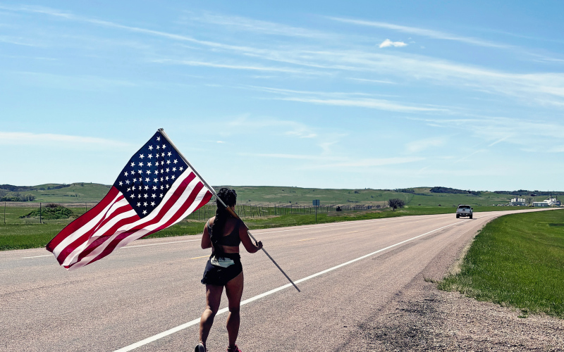 Carrying an American flag, Mai Richards continues west along Highway 34 near Wessington Springs during her cross-state Memorial Day tribute run. Richards plans to log nearly 450 miles across South Dakota while raising funds for veteran organizations.