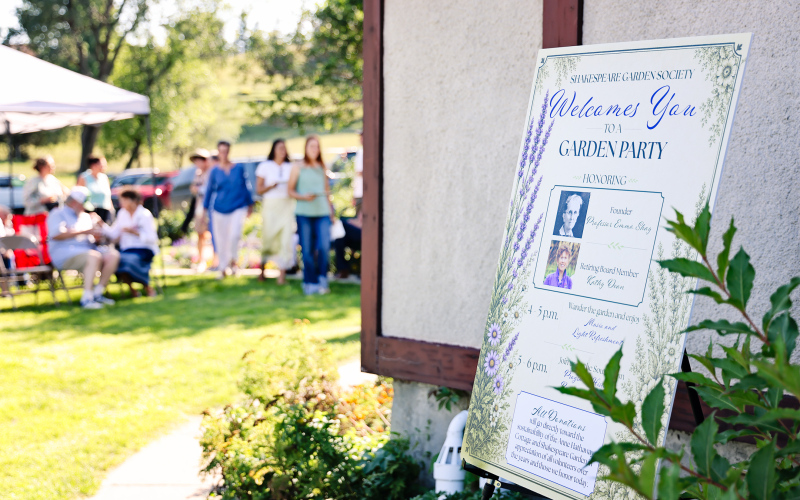 Signs featuring photos of Emma Shay and Dean welcome guests to the Garden Party celebrating a century of Shakespeare Garden history.