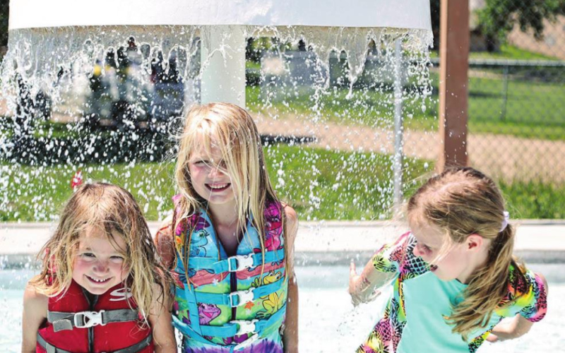 Shown left to right: Austen and Hayden Bultsma along with Alice Heumiller were the very first swimmers to splash in the newly constructed wading pool at the municipal swim area in the city park in Wessington Springs. New features including the mushroom fountain (pictured), floor bubbler and sprayers drew dozens of families to the pool on opening day last Thursday and over the hot weekend. KRISTI HINE / TRUE DAKOTAN