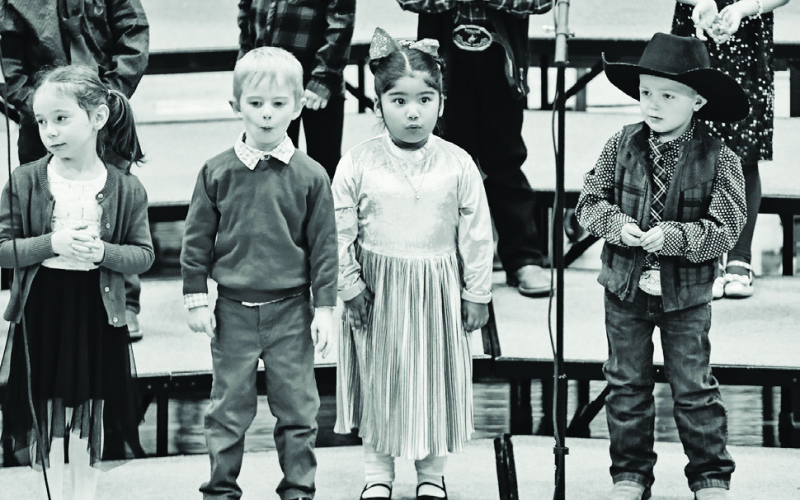 KRISTI HINE / TRUE DAKOTAN TOP: Kindergarten, first and second graders performed five songs during the elementary holiday concert last Friday. ABOVE RIGHT: Preschool students Finley Weber and Mayzie Miller belt out the lyrics to “Snowflakes, Snowflakes!” LEFT: Black felt cowboy hats were popular with preschool students this year, as can be seen during the class’ performance of “Christmas Action Song.”