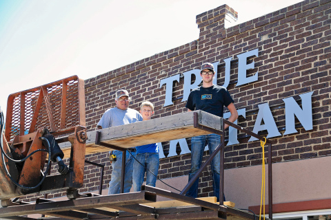 Craig Jensen, his grandson Sutten and Jensen Construction employee Xavier Baysinger made quick and precise work of hanging the metal sign made by the welding outfit at Spring Valley Colony.      