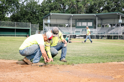 City of Wessington Springs employees Dylan Schimke and Lucas VanEnglenburg (foreground) work to repair a sprinkler at David Jost Memorial Field in preparation for this weekend’s amateur baseball district tournament. Cade Mohling (background) walks toward the mound to continue valve repairs. KRISTI HINE / TRUE DAKOTAN 