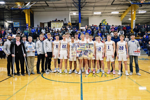 KRISTI HINE / TRUE DAKOTAN Wessington Springs High School junior Parker Graff (center), standing with his teammates and coaches in front of a home crowd, proudly displays a 1,000 point banner shortly after achieving the milestone at last week’s 70-31 victory over Hitchcock-Tulare.