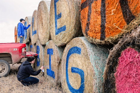 Teagan and Carissa Scheel carefully spray paint hay bales along Highway 281 with the inspiring “Go Blue, Love Big” message, that not only supports the Spartans but also honors the memory of the Spartans’ biggest fan, the late Lisa Bergeleen.