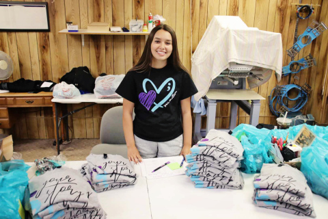 BENJAMIN CHASE / PLAINSMAN Huron High School senior Cadence Kogel sorts through stacks of the t-shirts that she worked with PB Sports to produce for Monday’s Day of Hope in Huron.
