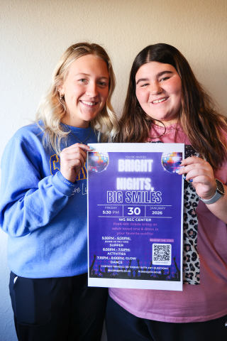 Wessington Springs High School students Kendall Kolousek, left, and Tierney Knipfer hold a flyer for Bright Nights, Big Smiles, a family engagement event they are organizing through the school’s FCCLA chapter. The glow-themed event will be held Jan. 30 at the WS Rec Center. (KRISTI HINE / TRUE DAKOTAN)