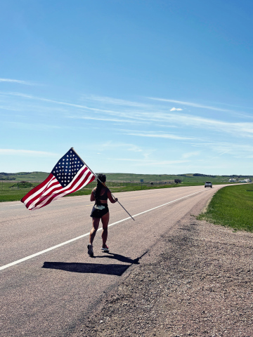 Carrying an American flag, Mai Richards continues west along Highway 34 near Wessington Springs during her cross-state Memorial Day tribute run. Richards plans to log nearly 450 miles across South Dakota while raising funds for veteran organizations.