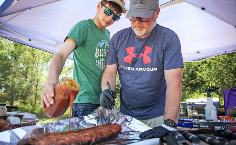 Father-son team Chris and Austin Schimke work together to apply homemade barbecue sauce.