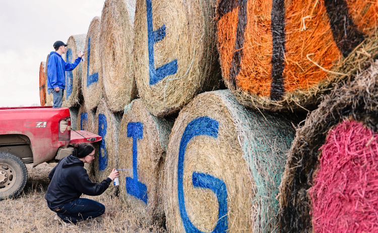 Teagan and Carissa Scheel carefully spray paint hay bales along Highway 281 with the inspiring “Go Blue, Love Big” message, that not only supports the Spartans but also honors the memory of the Spartans’ biggest fan, the late Lisa Bergeleen.