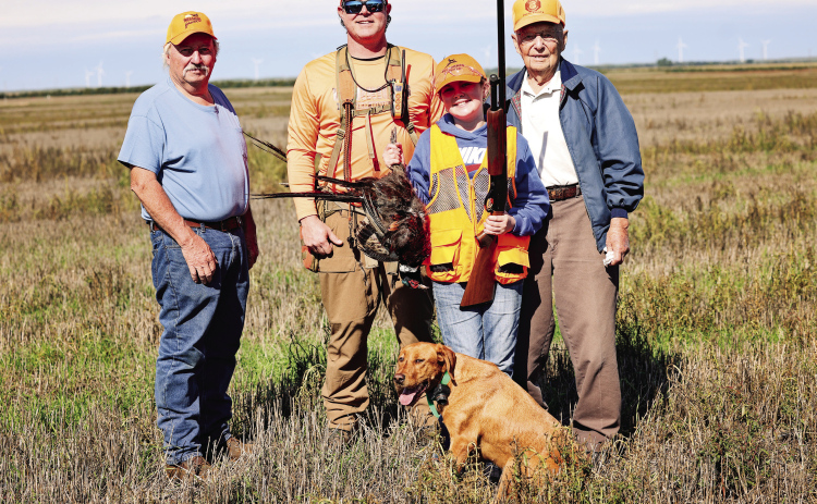 Four generations of hunting tradition come together following the Oct. 3 Pheasants Forever Youth Hunt. From left, Steve Winter, Jason Weber, Hadley Weber and Dayle Winter stand in the field with Hadley’s first pheasant. Hunting dog Minnie joins the group in front.